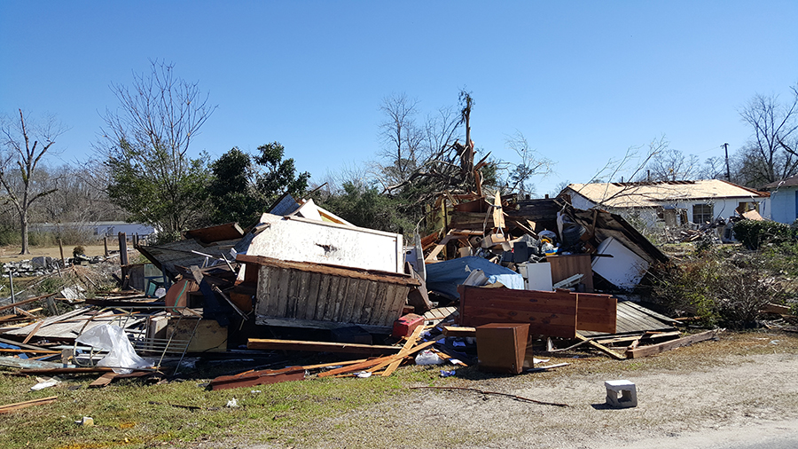 A storm-damaged home leaves debris including furniture and wood on the property.