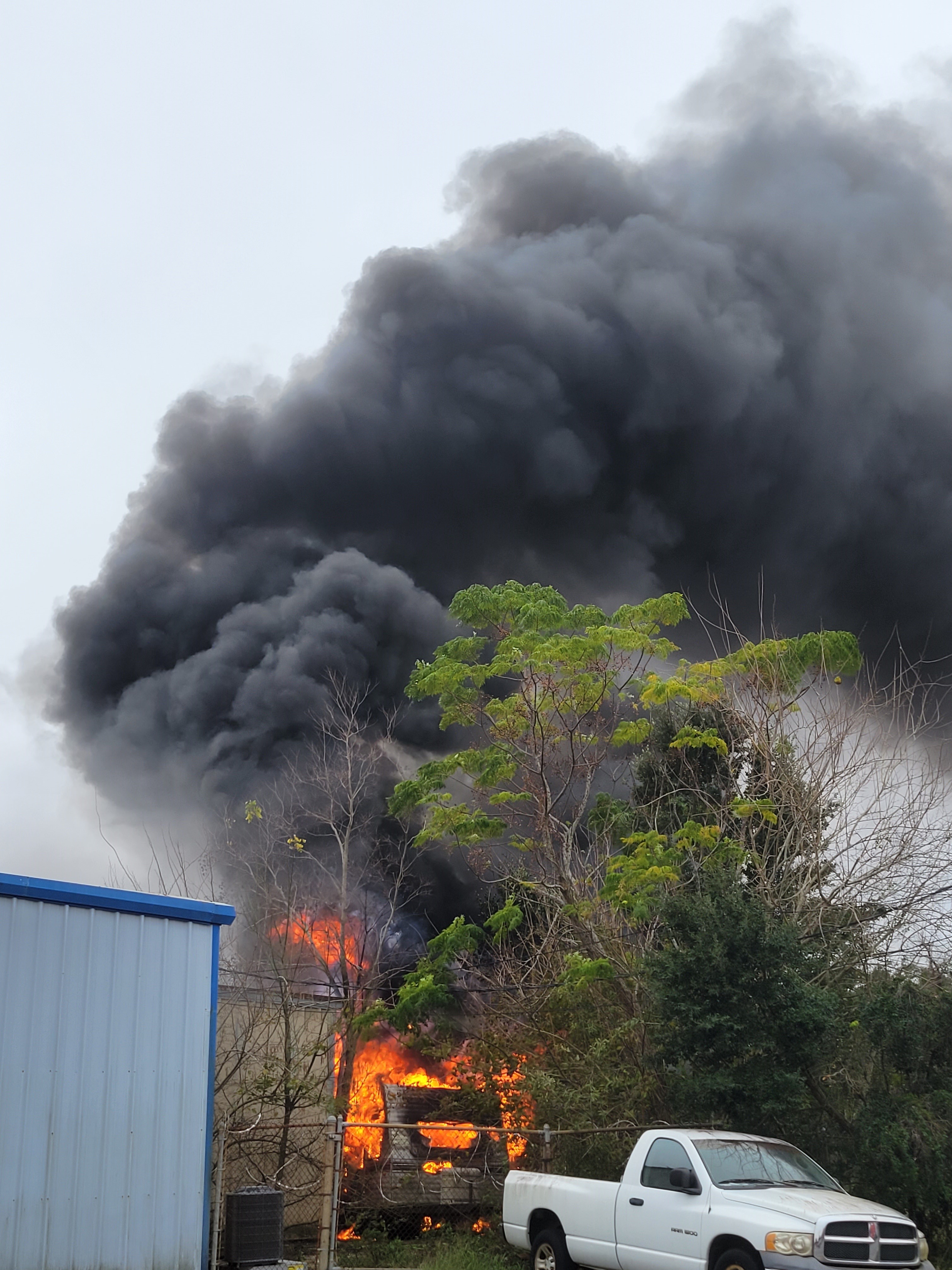 An RV camper trailer fully engulfed in flames.