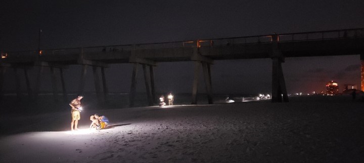 People using white lights on the beach at night